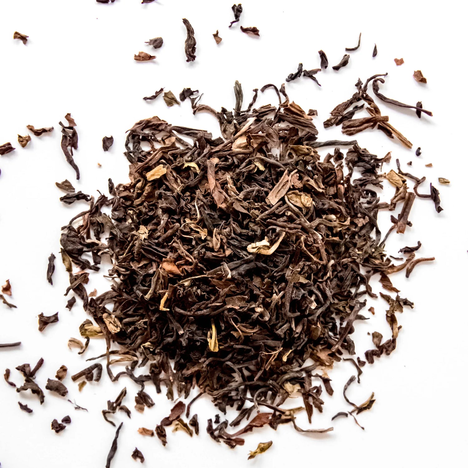 Loose leaf Darjeeling black tea with curled leaves scattered on white background, by Yerba Buena Tea Company.