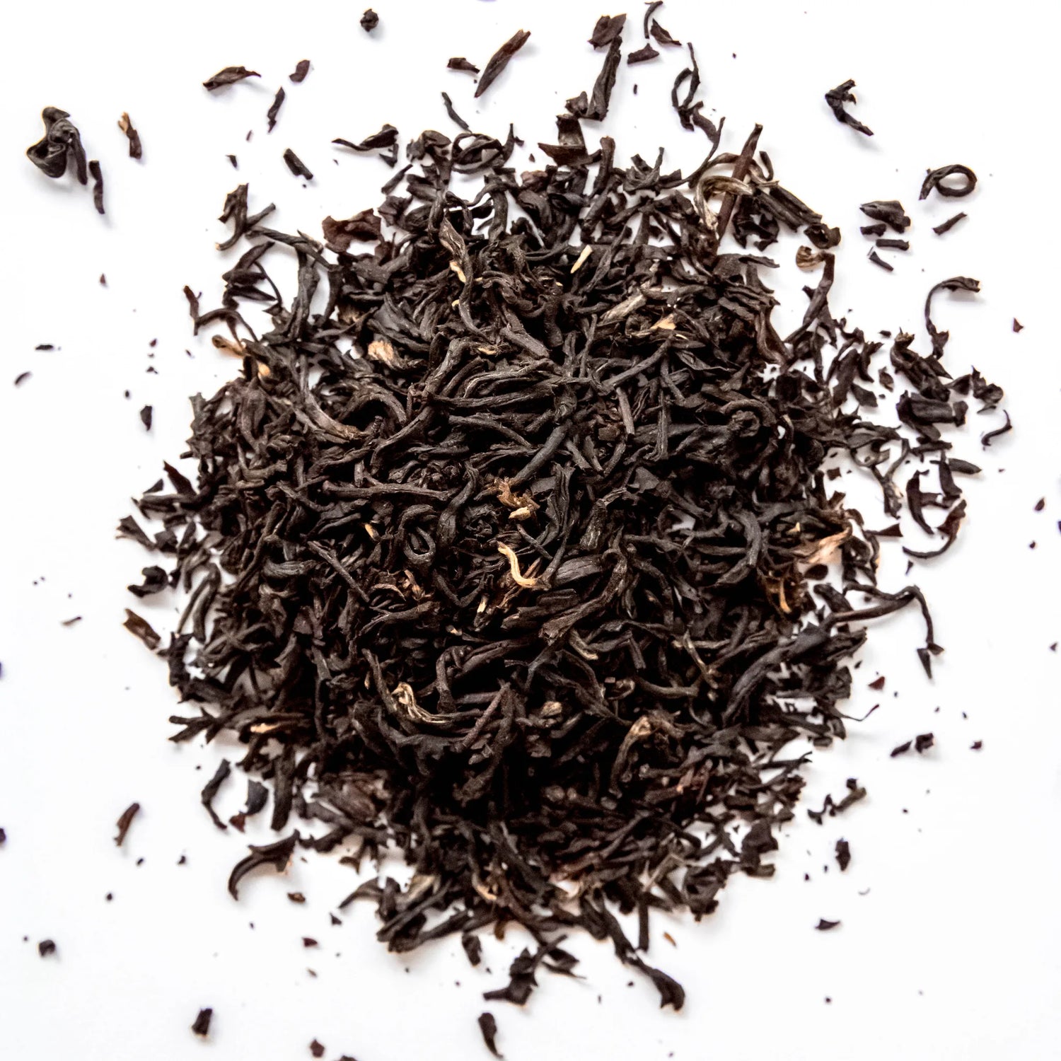 Loose leaf Earl Grey black tea with curled leaves scattered on white background, by Yerba Buena Tea Company.