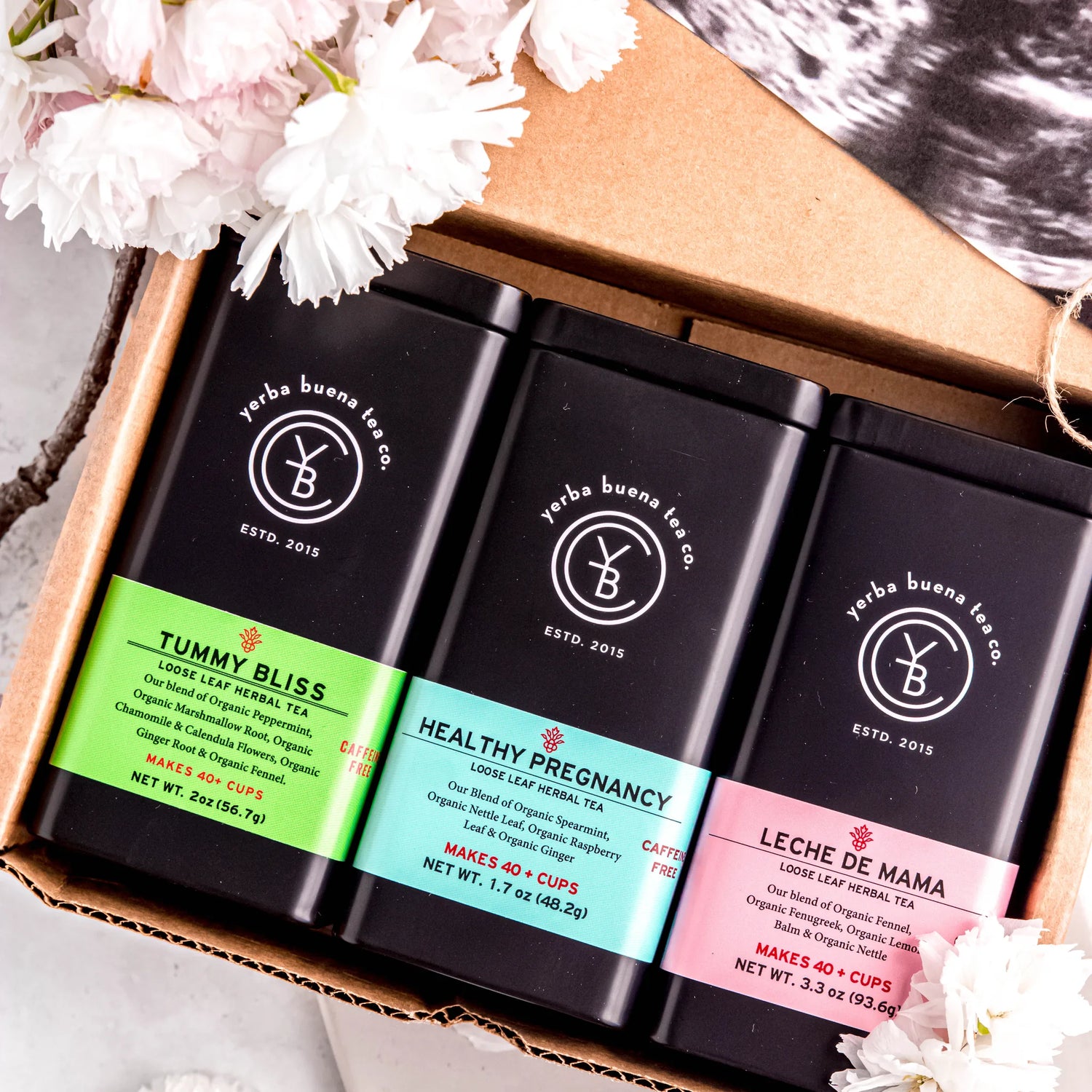The Expecting Mothers Box Set gift featuring three loose leaf herbal teas: Tummy Bliss, Healthy Pregnancy, and Leche de Mama in branded pouches, nestled in kraft packaging with pink and white flowers, by Yerba Buena Tea Company.
