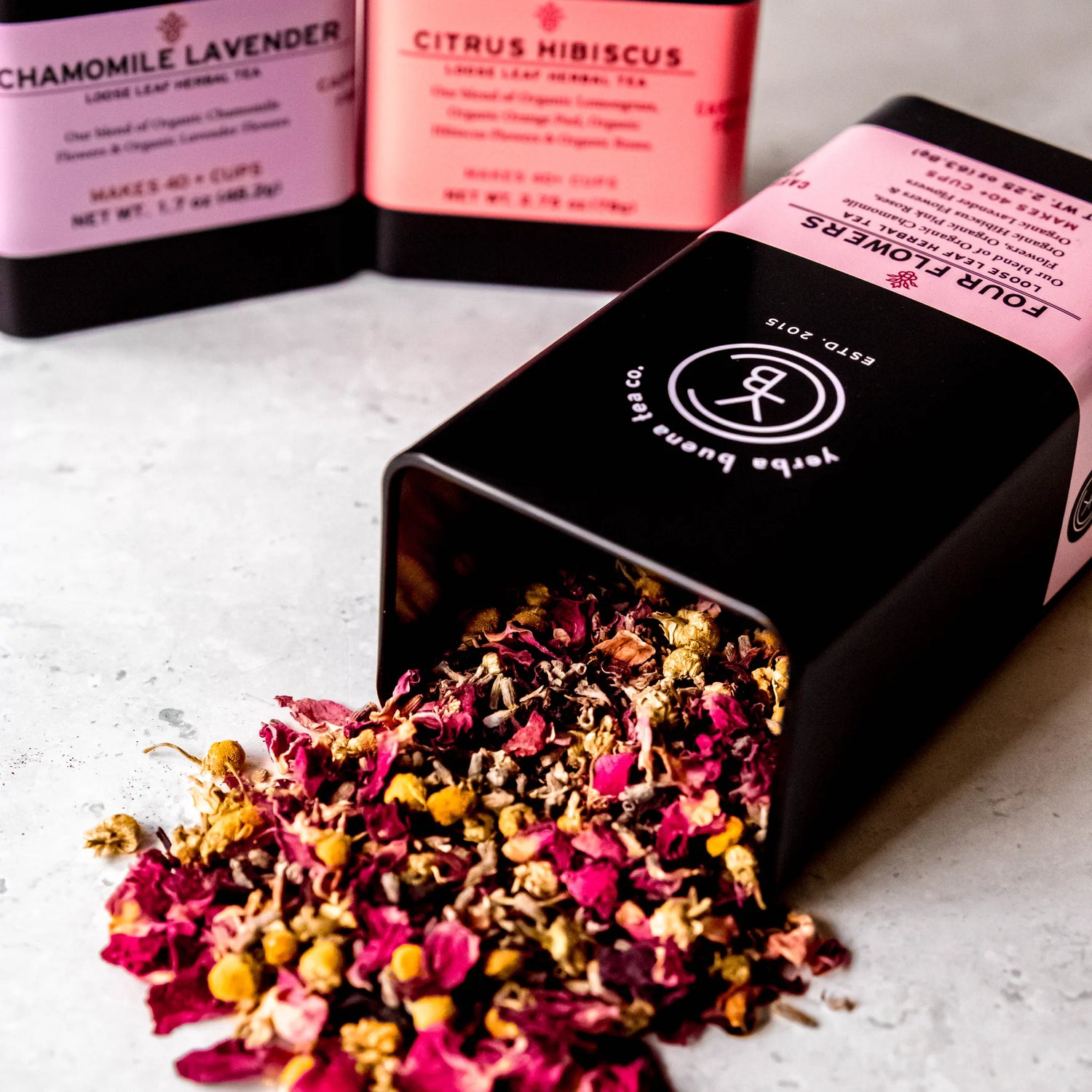 Floral Box Set gift displaying loose leaf herbal teas including Chamomile Lavender and Citrus Hibiscus in pink and coral pouches with colorful dried petals spilling from an open box, by Yerba Buena Tea Company.