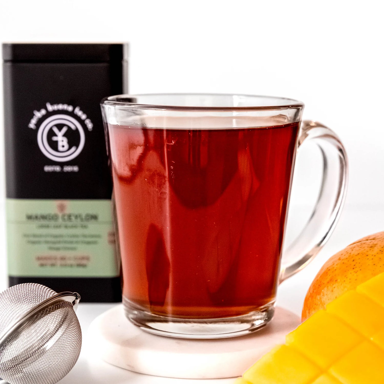 Brewed Mango Ceylon black tea in clear glass mug beside packaged tea pouch, by Yerba Buena Tea Company.