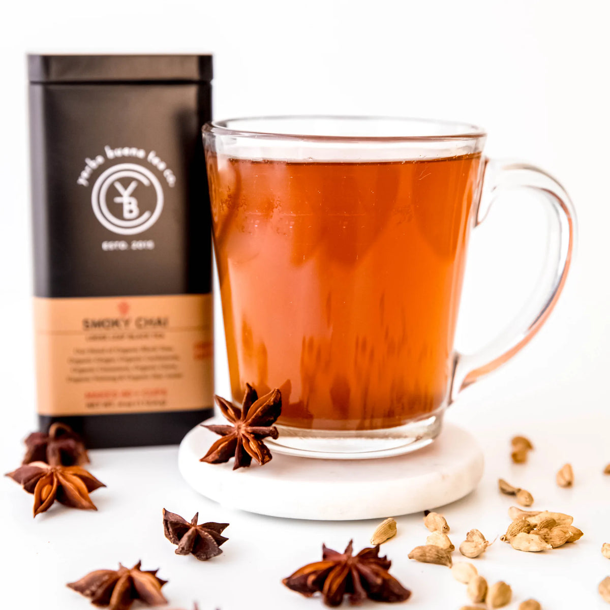 Smoky Chai loose leaf tea brewed in clear glass mug with star anise and cardamom pods scattered nearby, by Yerba Buena Tea Company.