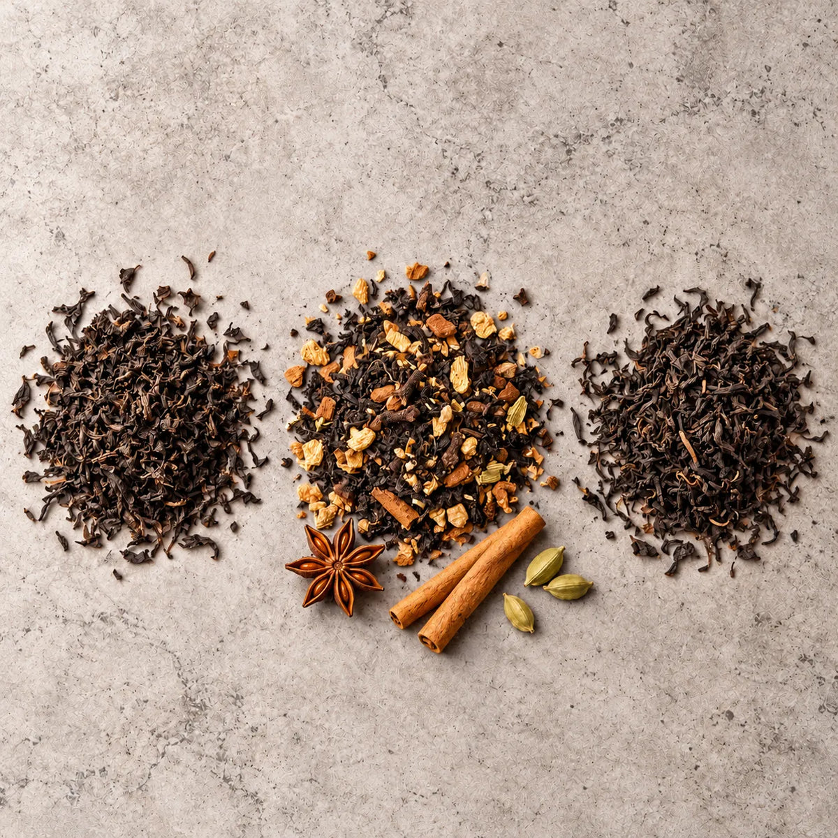 Loose Lapsang Souchong and Assam on either side of a pile of Smoky Chai, with star anise, cinnamon sticks and cardamom pods on stone