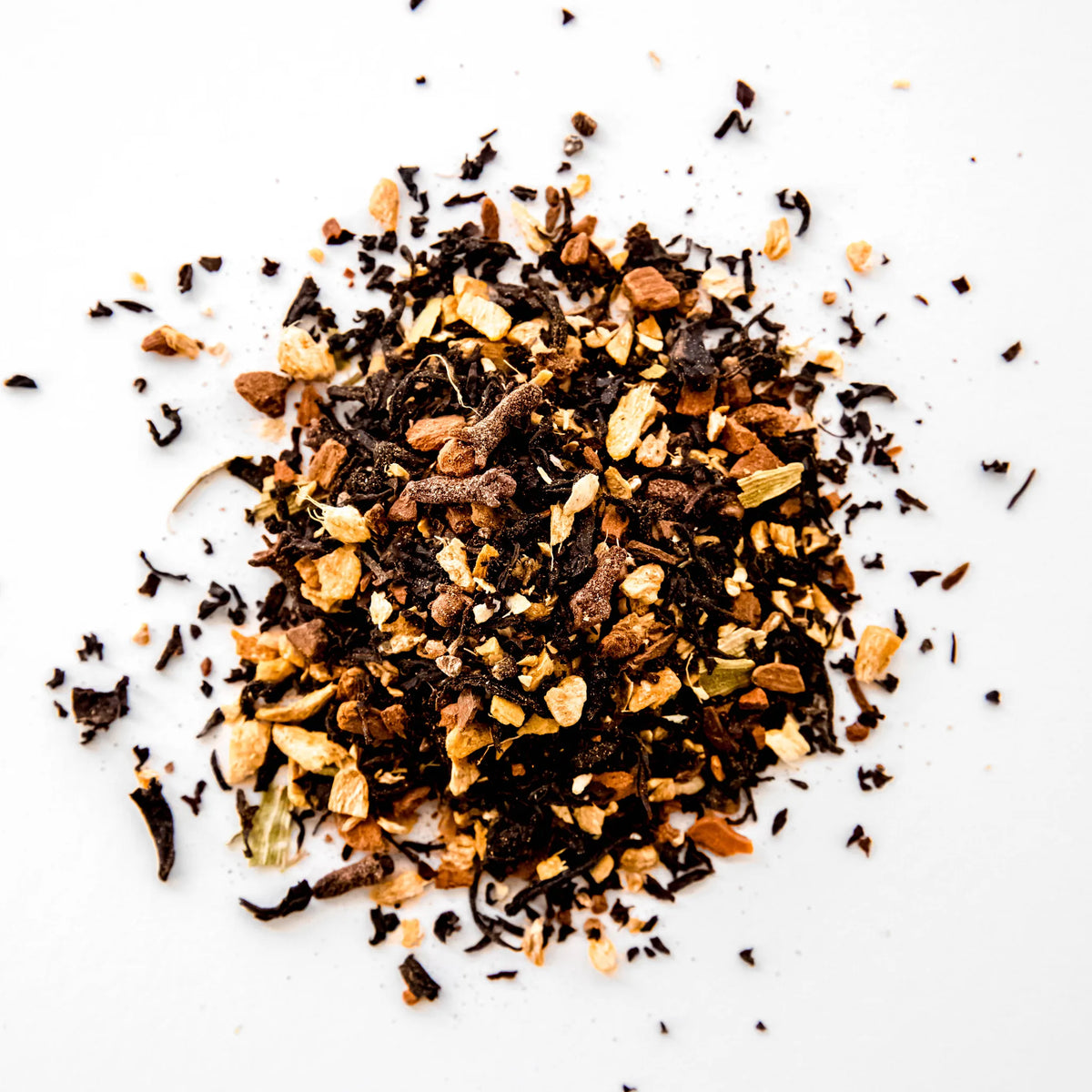 Loose leaf Smoky Chai blend with dark tea leaves and warm spice fragments scattered on white background, by Yerba Buena Tea Company.