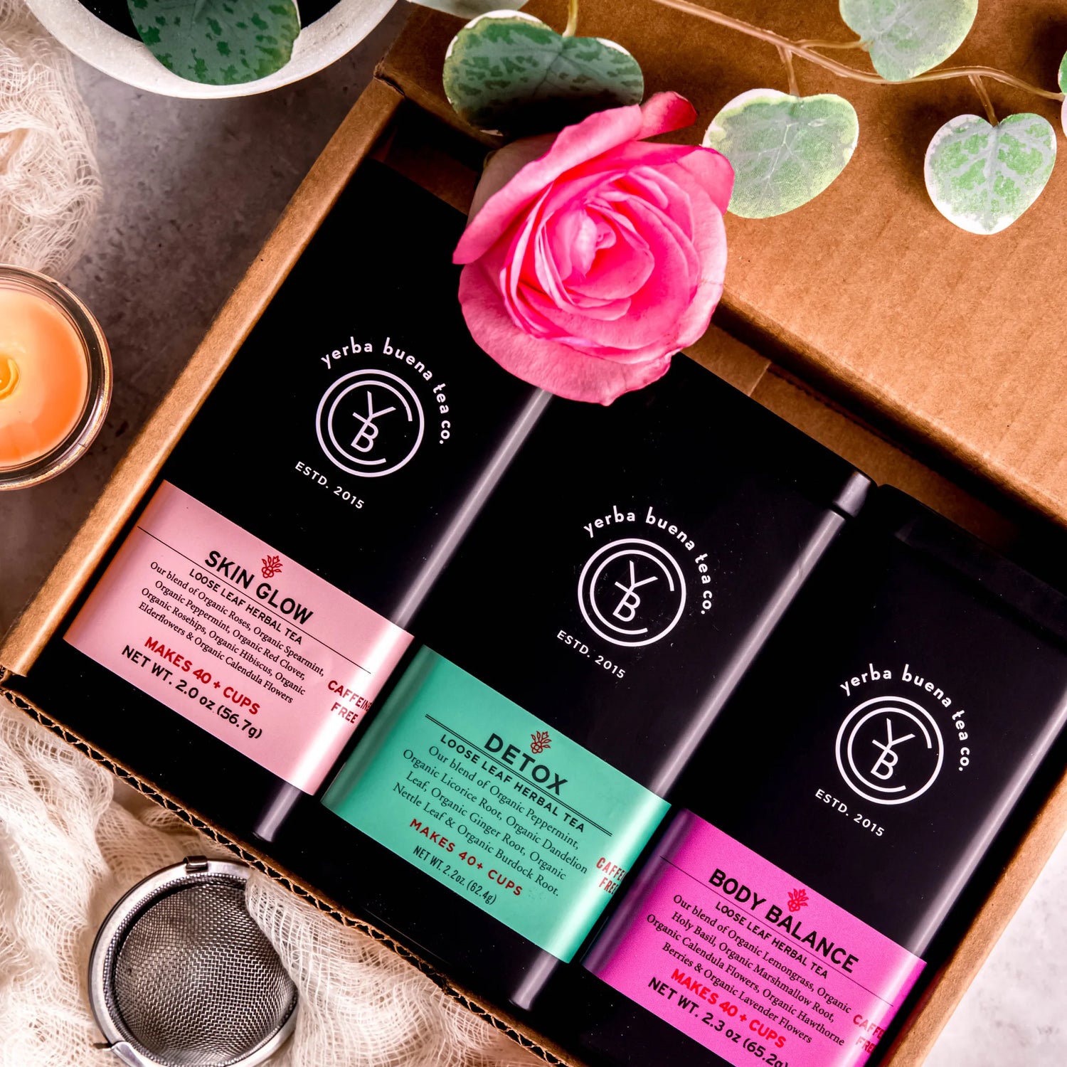 The Wellness Self Care Box Set gift featuring three herbal tea pouches labeled Skin Glow, Detox, and Body Balance arranged in a wooden box with fresh flowers and greenery, by Yerba Buena Tea Company.
