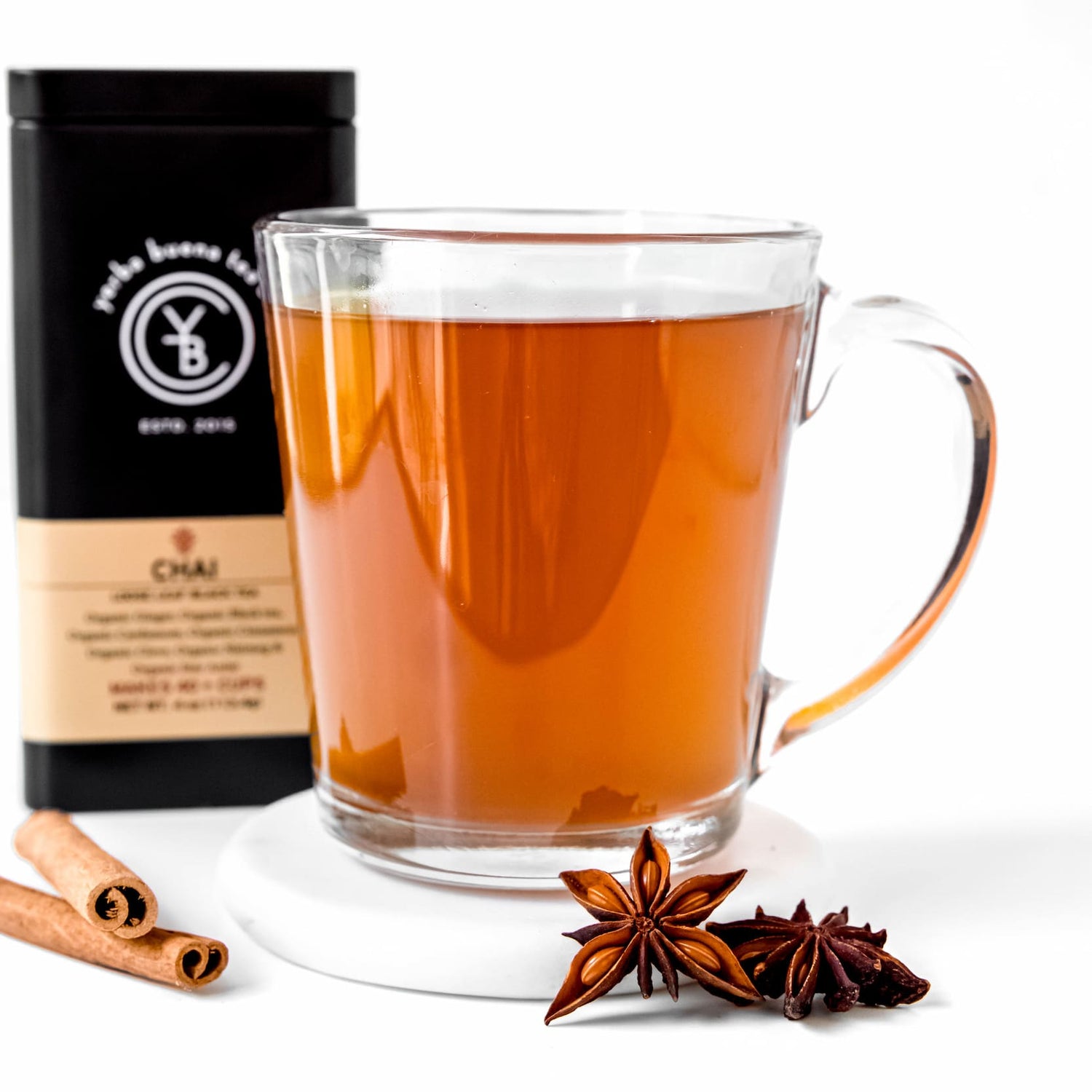 A clear glass mug of brewed organic Chai tea from Yerba Buena Tea Co., with cinnamon sticks and star anise in the foreground.