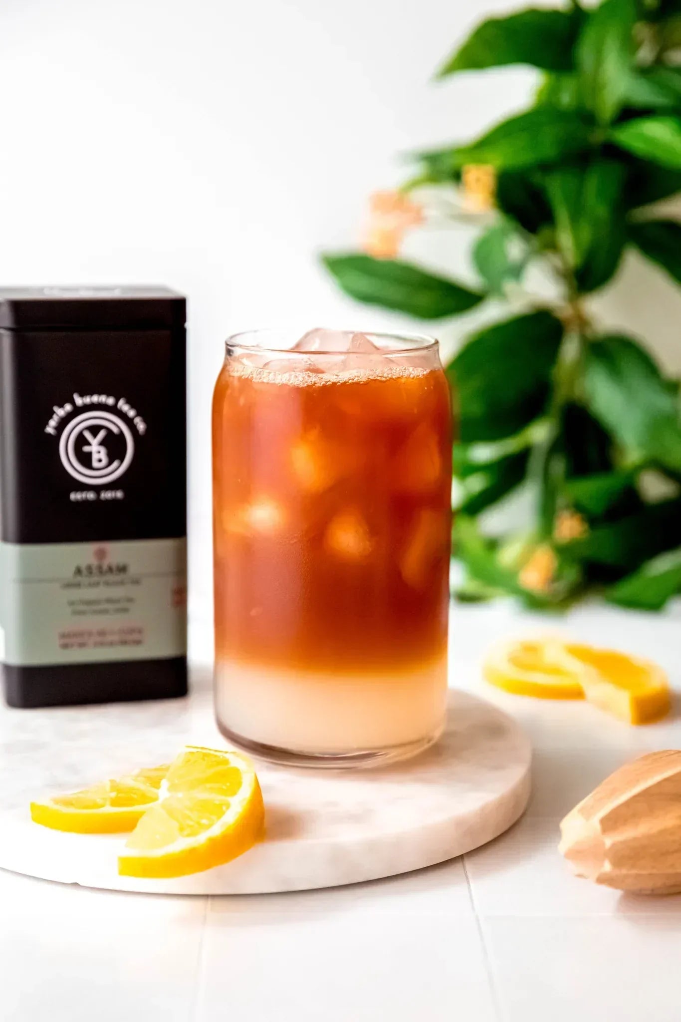 Iced Assam Arnold Palmer tea with creamy bottom layer and amber top, garnished with lemon slices on marble coaster, from Yerba Buena Tea Company.