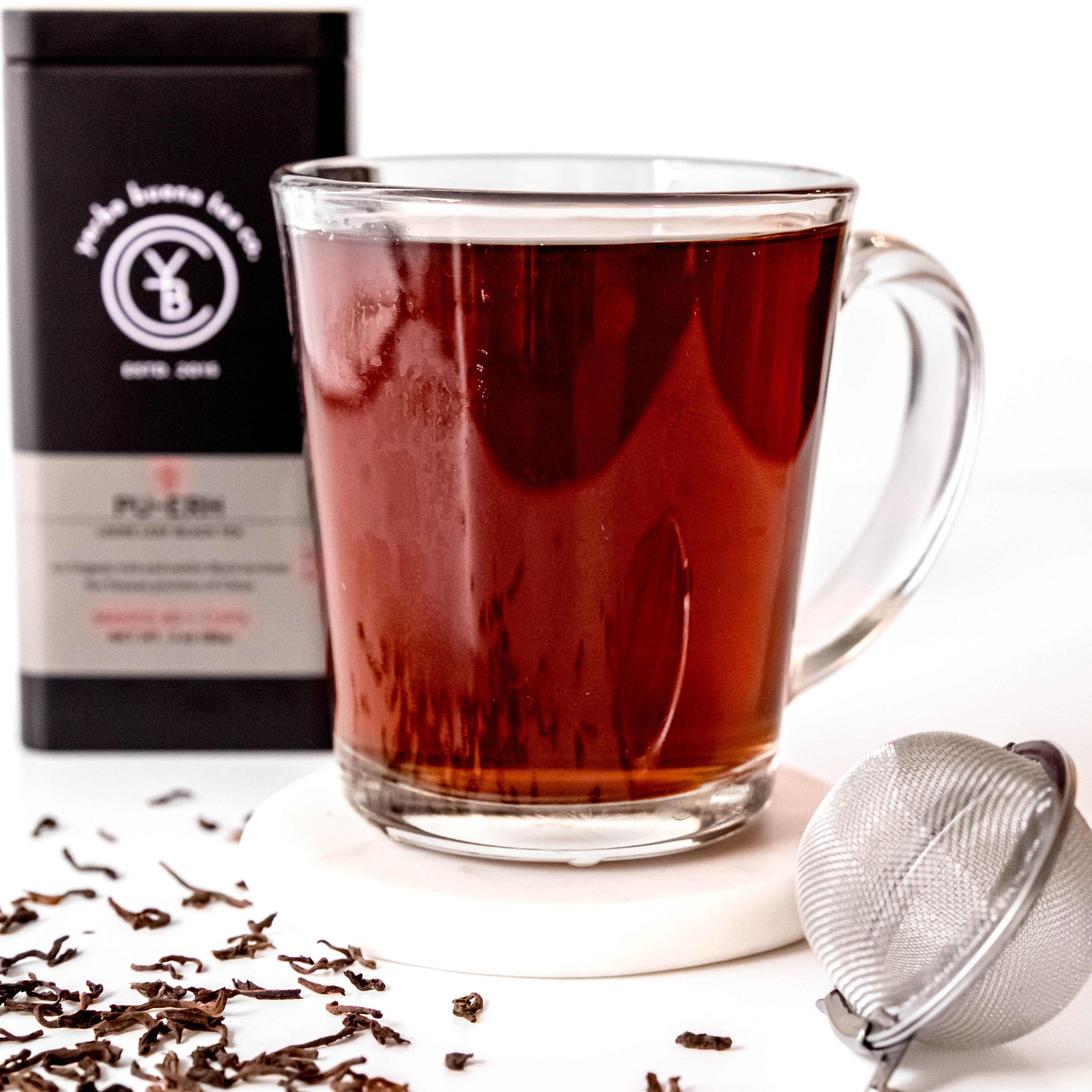 A cup of brewed Pu'erh Tea with a deep reddish-brown hue, exuding an earthy and smoky aroma.