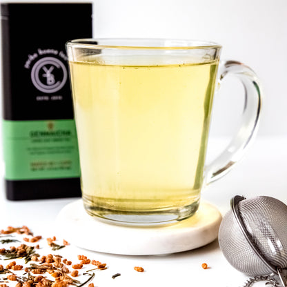 A cup of brewed Genmaicha tea with a light golden hue, surrounded by loose-leaf ingredients.