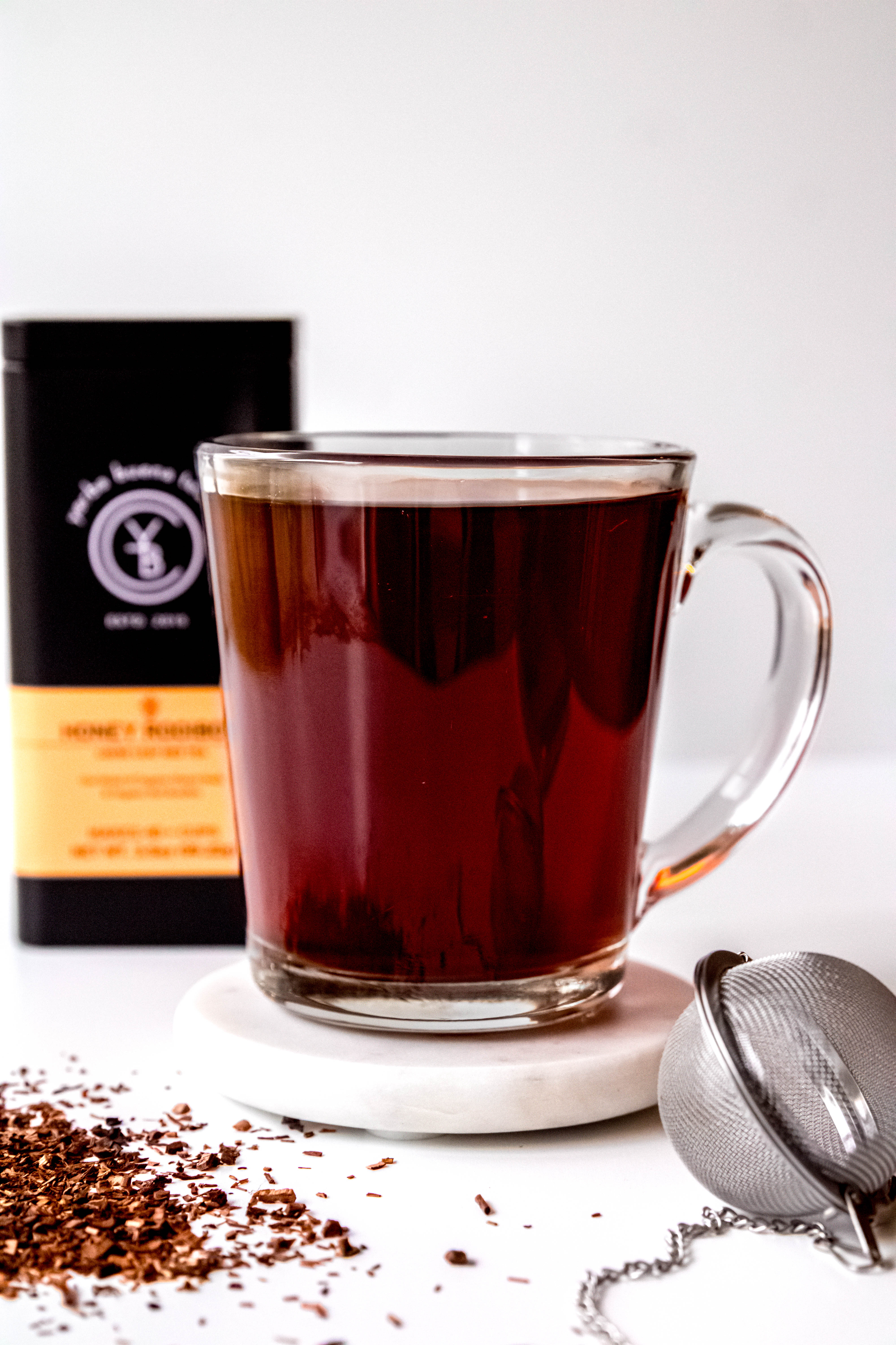 A cup of brewed Honey Rooibos tea with a rich amber hue, surrounded by loose-leaf ingredients.