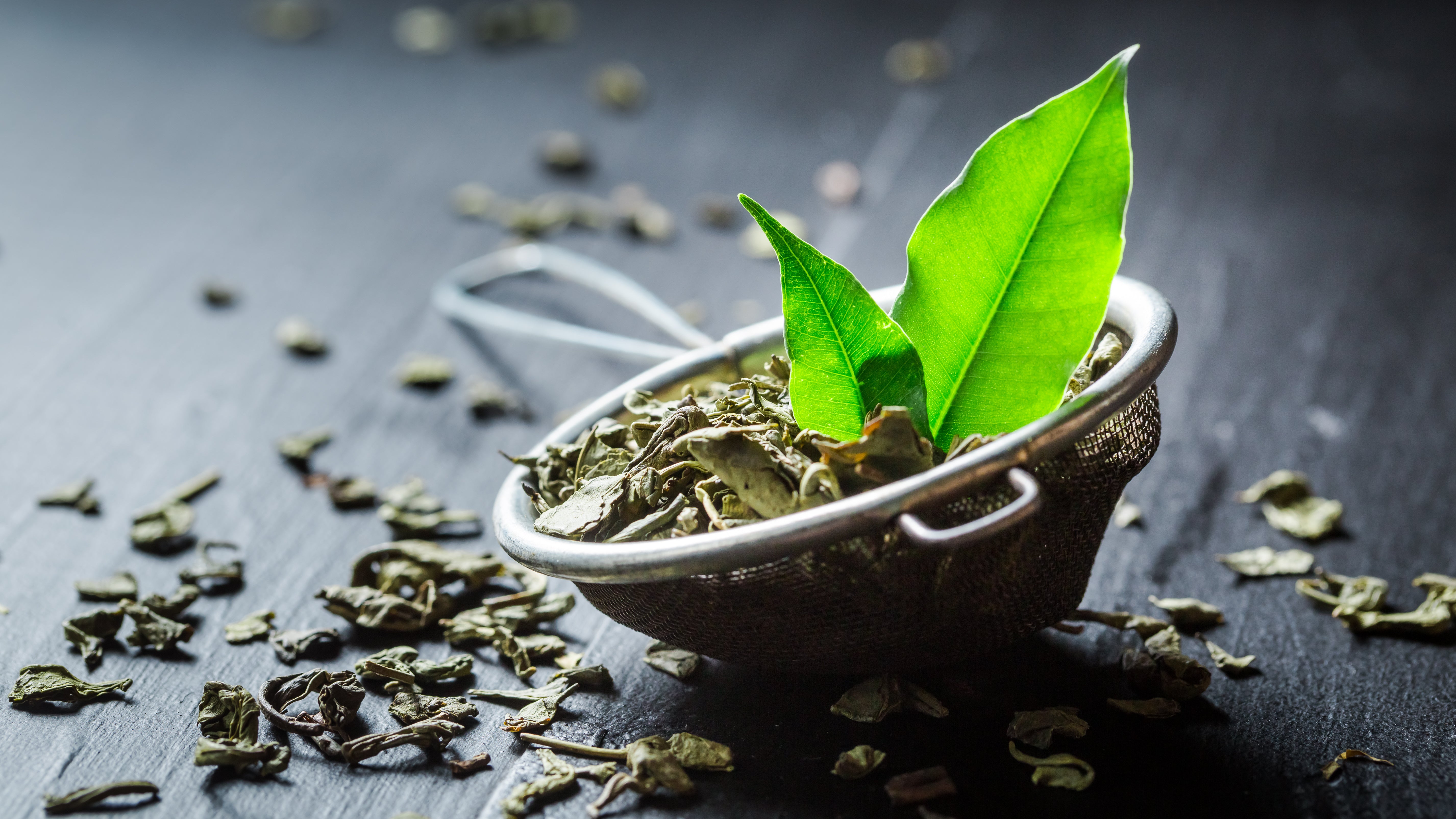 Loose green tea leaves scattered with a fresh green leaf on a wooden surface. Discover premium loose-leaf green tea at Yerba Buena Tea Co. for a refreshing and healthy tea experience.