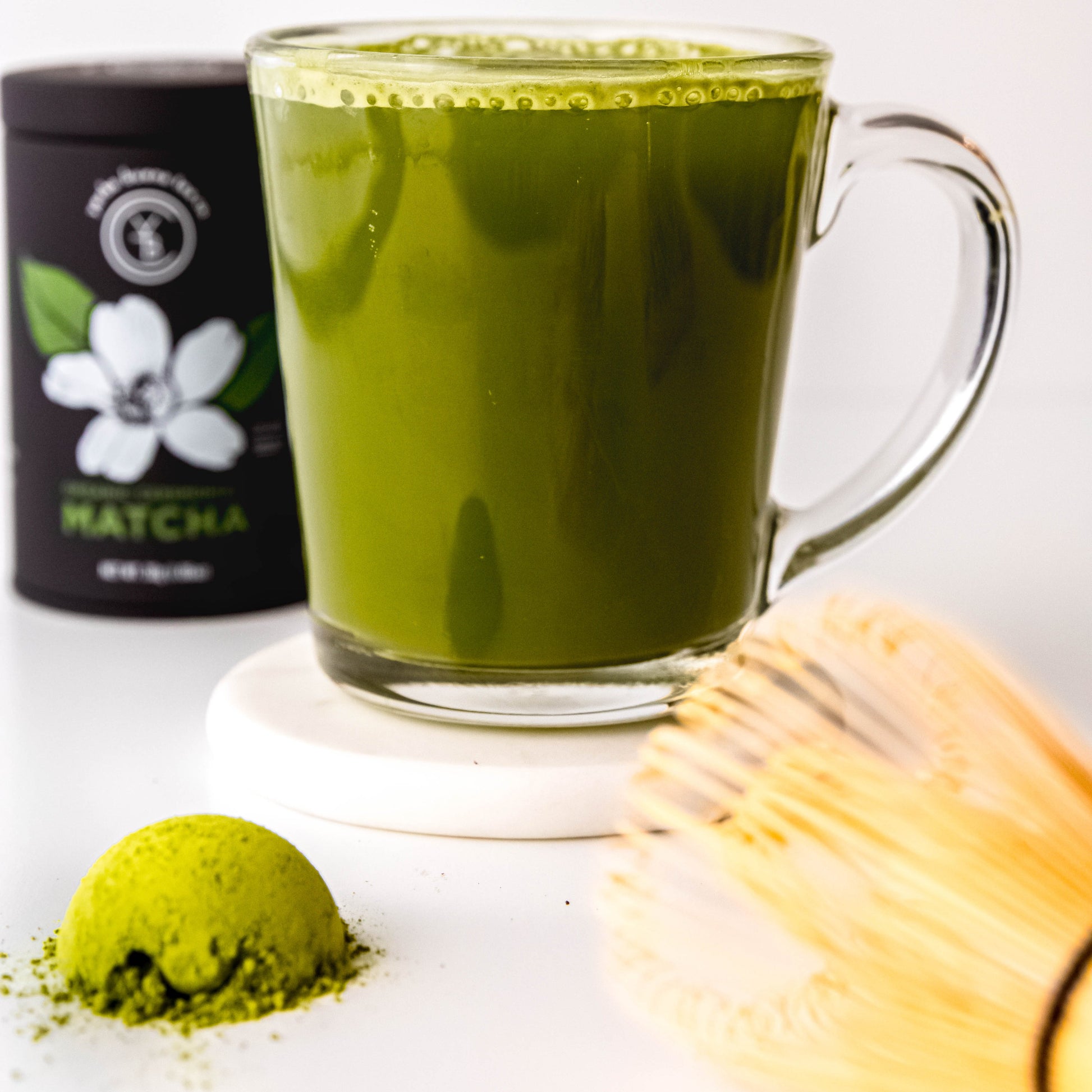 A frothy cup of Ceremonial Matcha surrounded by matcha tools and vibrant green powder.