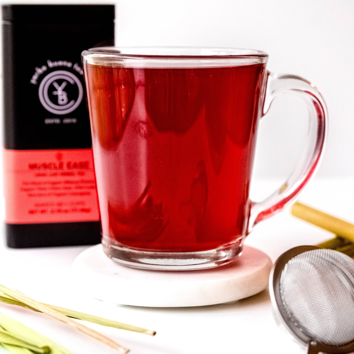 A cup of brewed Muscle Ease tea with a vibrant red hue, surrounded by loose-leaf ingredients.