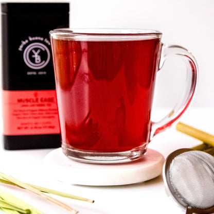 A cup of brewed Muscle Ease tea with a vibrant red hue, surrounded by loose-leaf ingredients.