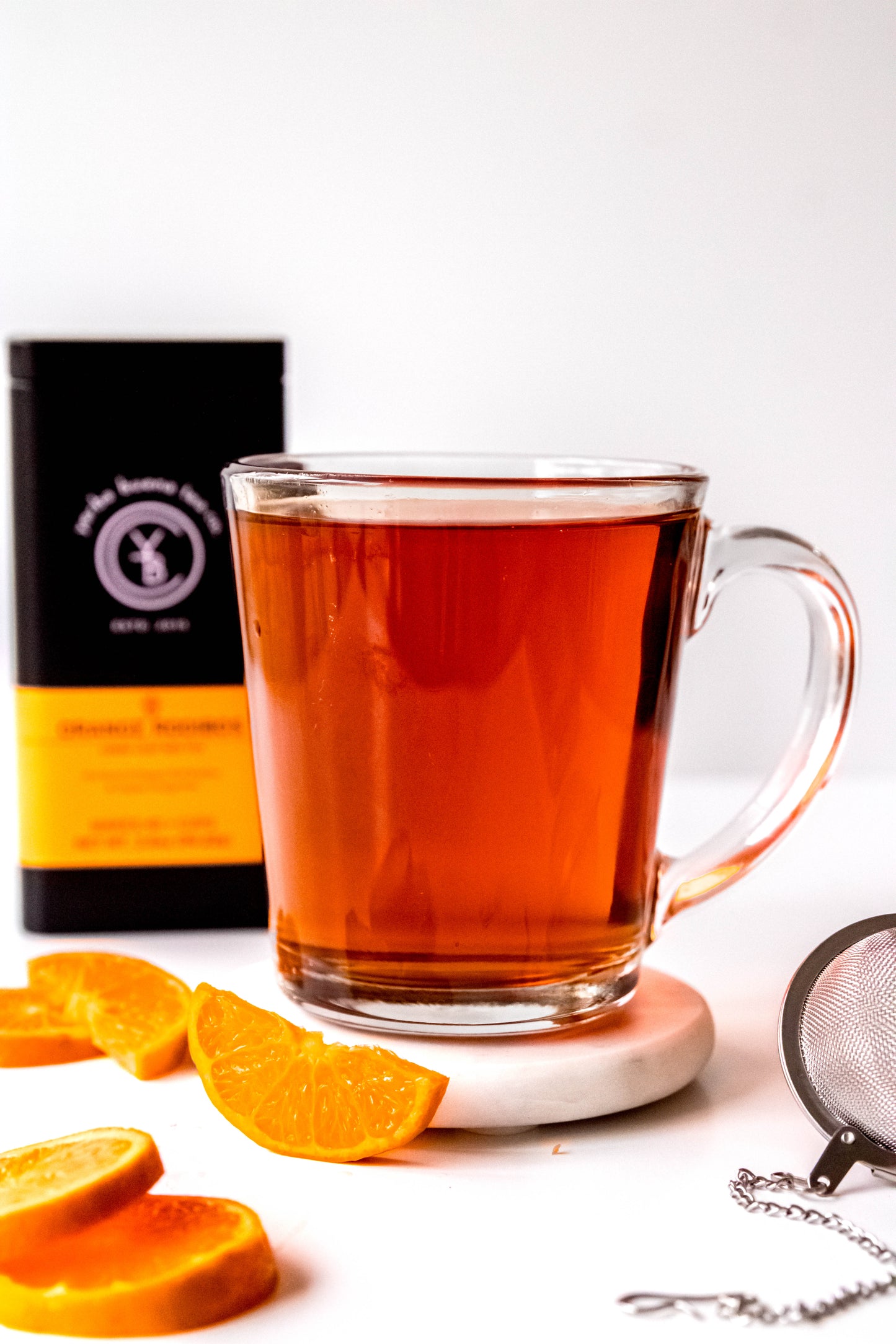 A cup of brewed Orange Rooibos tea with a rich amber hue, surrounded by loose-leaf ingredients.