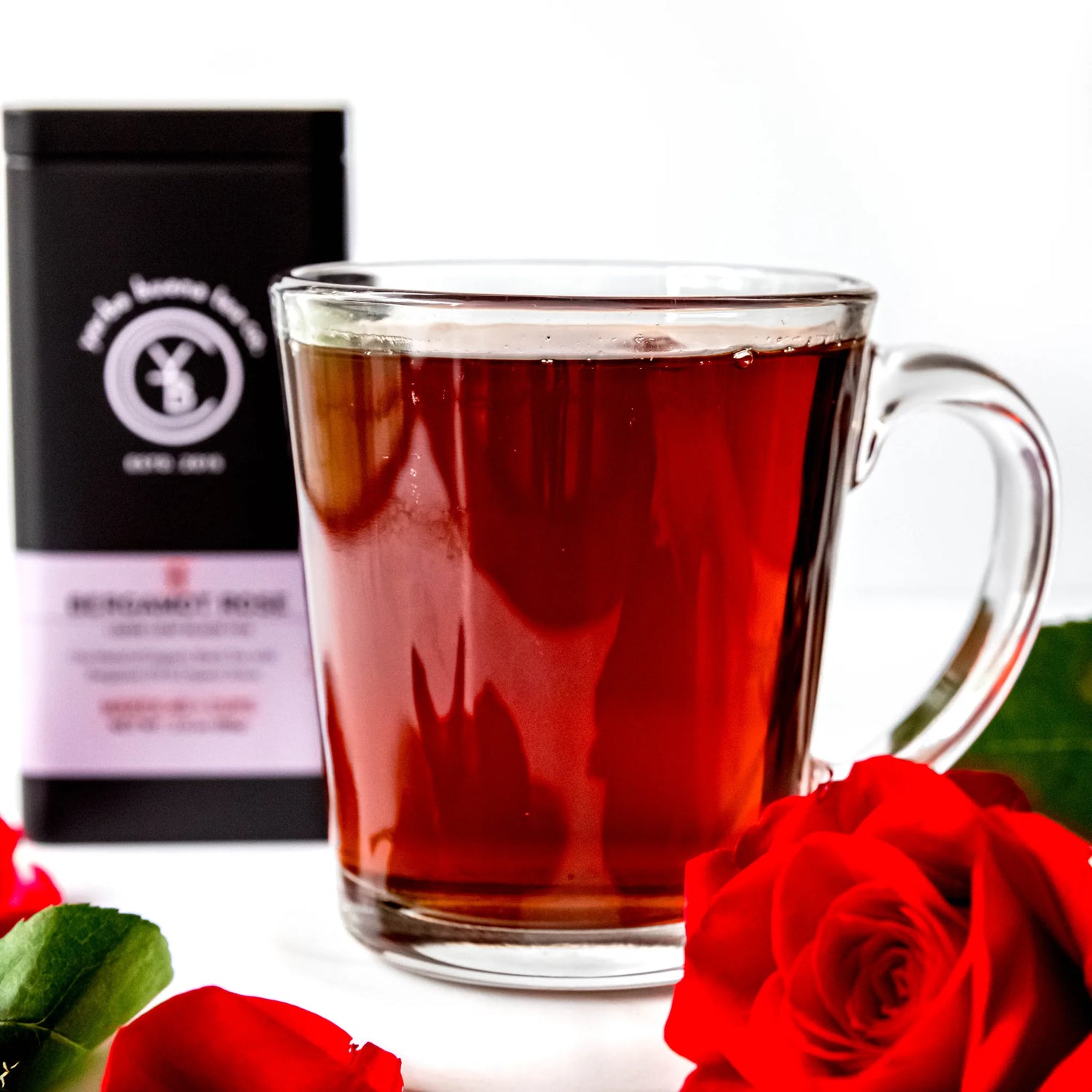 Brewed red tea in glass mug with fresh roses and black packaging pouch behind, by Yerba Buena Tea Company.