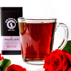 Brewed red tea in glass mug with fresh roses and black packaging pouch behind, by Yerba Buena Tea Company.