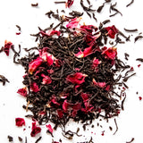 Loose leaf black tea with vibrant red rose petals scattered on white background, by Yerba Buena Tea Company.