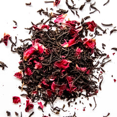 Loose leaf black tea with vibrant red rose petals scattered on white background, by Yerba Buena Tea Company.