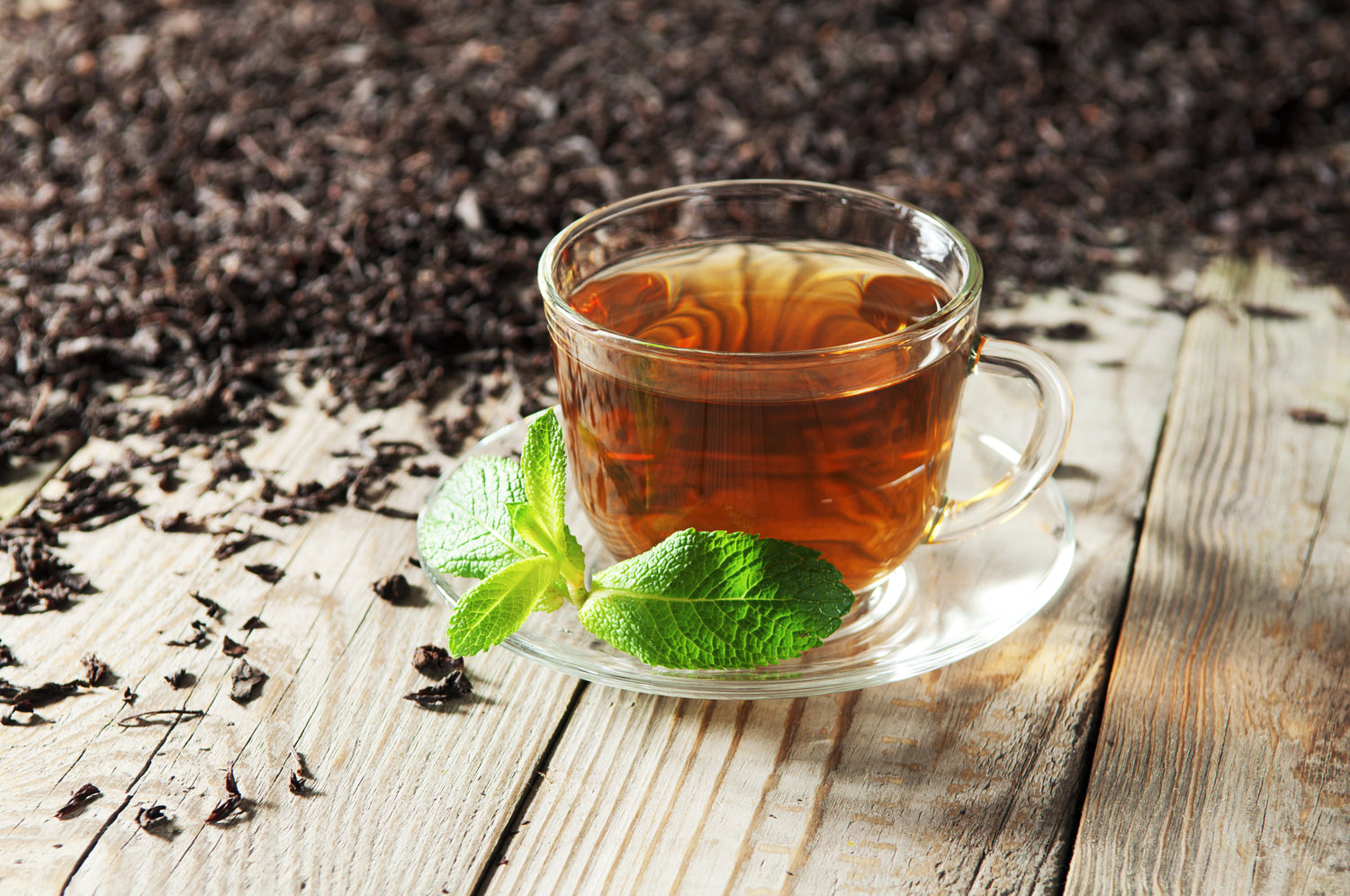 Cup of black tea with loose black tea leaves on a wooden surface. Explore the rich flavors of premium loose-leaf black tea at Yerba Buena Tea Co.