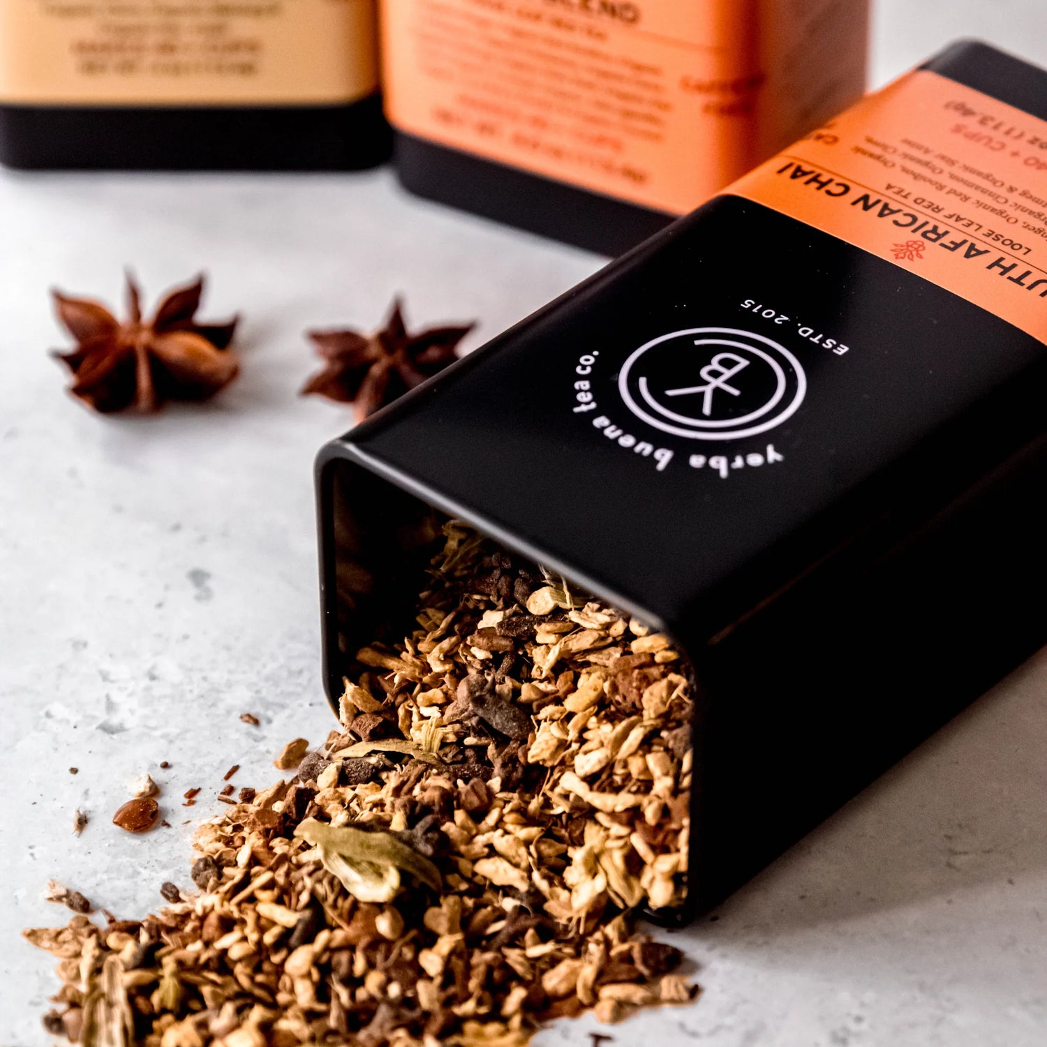 Chai Box gift set with loose leaf tea pouches in orange and black packaging, displayed with star anise and scattered tea leaves on a white surface, by Yerba Buena Tea Company.