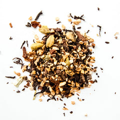 Loose leaf chai tea blend with dark tea leaves, cardamom pods, and spice pieces scattered on white background, by Yerba Buena Tea Company.