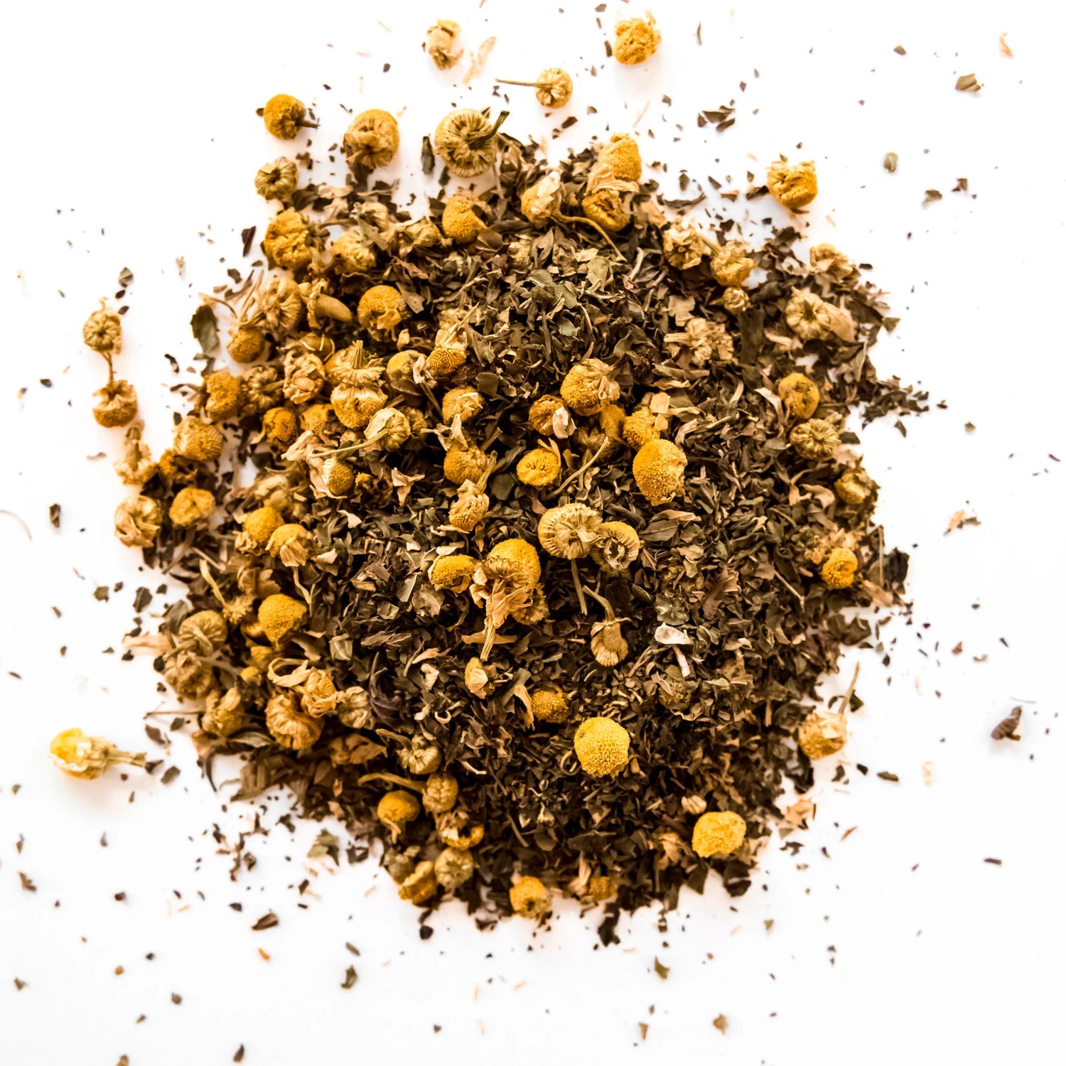 Loose leaf chamomile mint tea blend with dried chamomile flowers and green leaf pieces scattered on white background, by Yerba Buena Tea Company.