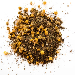 Loose leaf chamomile mint tea blend with dried chamomile flowers and green leaf pieces scattered on white background, by Yerba Buena Tea Company.