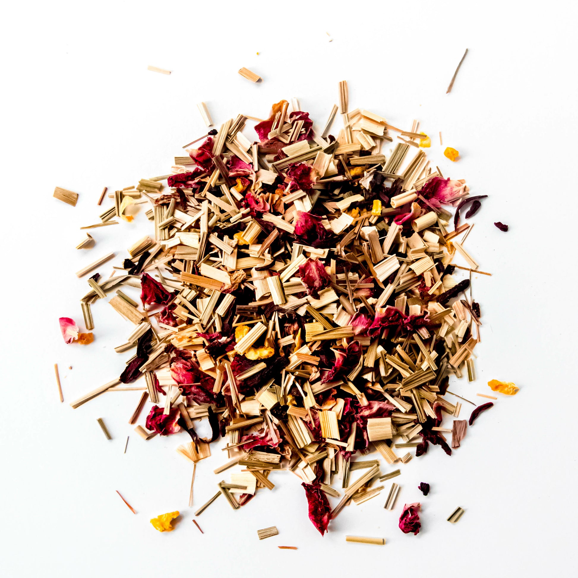 A close-up of the loose leaf blend of Citrus Hibiscus tea, showing the finely chopped organic lemongrass, orange peel, hibiscus, and roses against a white background.