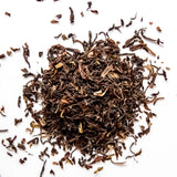 Loose leaf Darjeeling black tea with curled leaves scattered on white background, by Yerba Buena Tea Company.