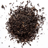 Loose leaf Earl Grey black tea with curled leaves scattered on white background, by Yerba Buena Tea Company.
