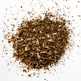 Loose leaf herbal tea blend with dried herbs and botanicals scattered on white background, by Yerba Buena Tea Company.