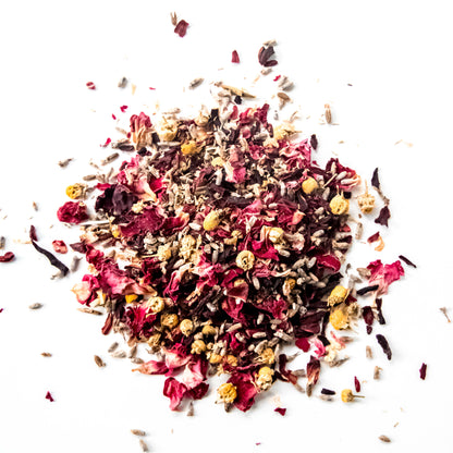 A close-up of the loose leaf blend of Four Flowers tea, showing the finely chopped organic chamomile, pink roses, hibiscus, and lavender flowers against a white background.