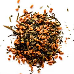 Loose leaf genmaicha tea blend with green tea leaves and roasted rice kernels scattered on white background, by Yerba Buena Tea Company.