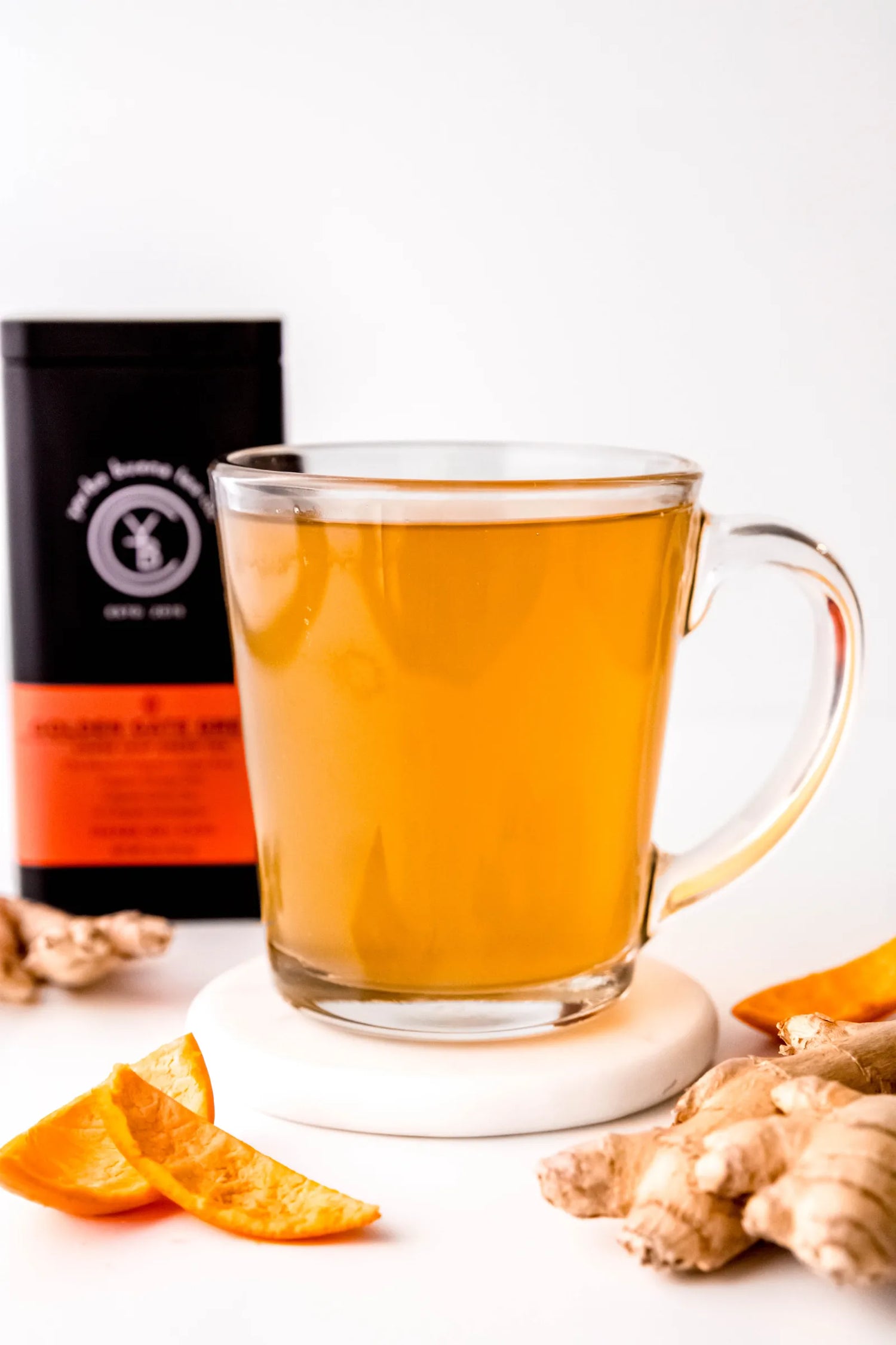 Clear glass mug filled with brewed Golden Gate Green organic green tea, warm golden in color, resting beside fresh ginger root and orange slices. A bright, citrus-forward green tea ritual handcrafted by Yerba Buena Tea Co.