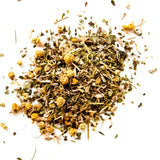 Loose leaf herbal tea blend with chamomile flowers and mint scattered on white background, by Yerba Buena Tea Company.