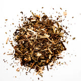 Loose leaf green tea blend with dried herbs and wood chips scattered on white background, by Yerba Buena Tea Company.