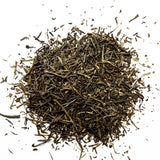 Loose leaf green sencha tea scattered on white background in natural dried leaf form, by Yerba Buena Tea Company.