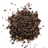 Loose leaf jasmine green tea with curled leaves scattered on white background, by Yerba Buena Tea Company.