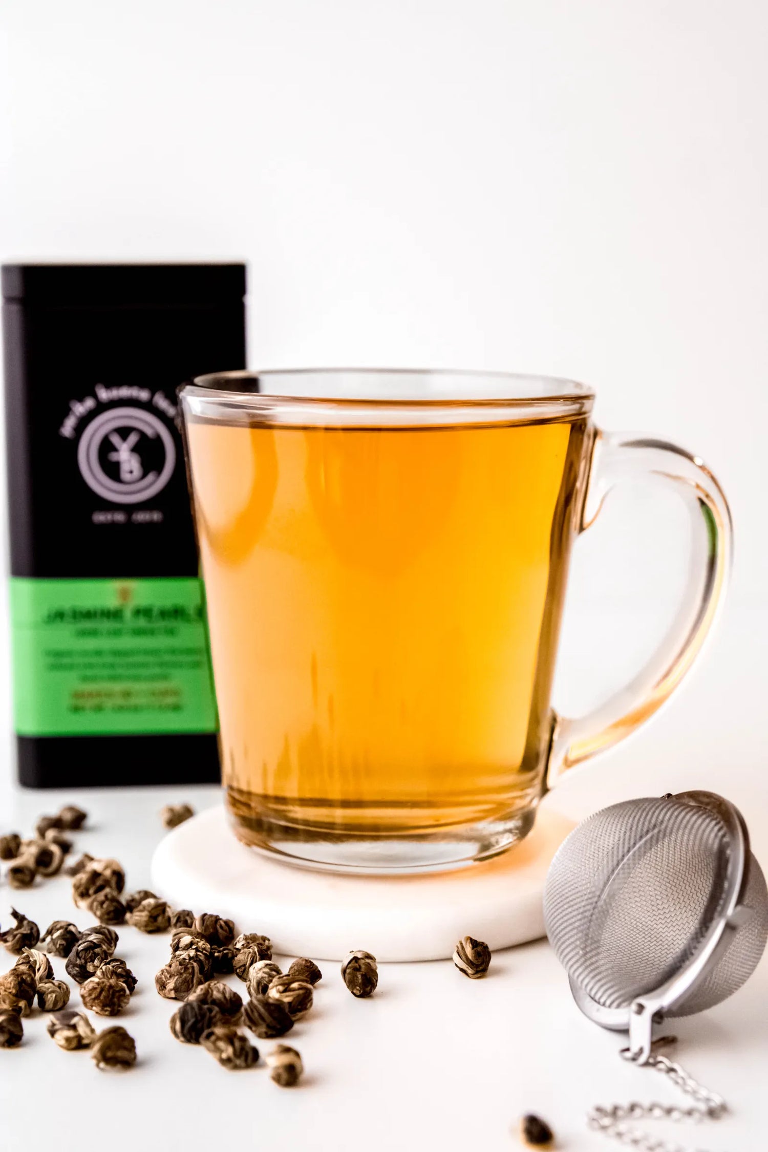 Clear glass mug filled with brewed Jasmine Pearls organic green tea, glowing golden in color and resting on a white coaster. A delicate jasmine-infused green tea ritual handcrafted by Yerba Buena Tea Co.