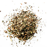 Loose leaf herbal tea blend with dried herbs, seeds, and botanicals scattered on white background, by Yerba Buena Tea Company.