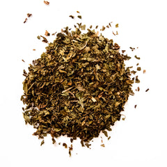 Loose leaf Northwest Mint herbal tea with green and golden dried leaves scattered on white background, by Yerba Buena Tea Company.