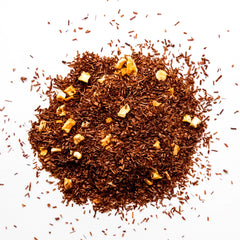 Loose leaf rooibos tea with dried orange pieces scattered on white background, by Yerba Buena Tea Company.