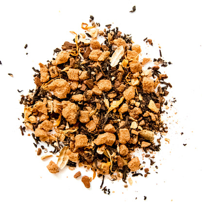 A close-up of the loose leaf blend of Pumpkin Spice tea, showing the mix of organic Assam black tea, cinnamon, crystallized ginger, cardamom, pumpkin spice, and marigold flowers against a white background.