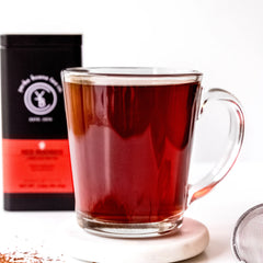 Brewed red rooibos tea in clear glass mug with black packaging box behind it, by Yerba Buena Tea Company.