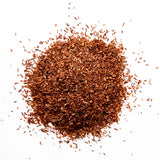 Loose leaf red rooibos tea scattered in a pile against a white background, by Yerba Buena Tea Company.