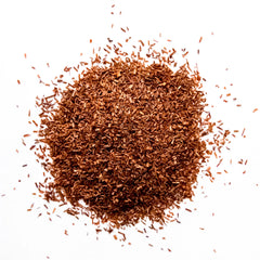 Loose leaf red rooibos tea scattered in a pile against a white background, by Yerba Buena Tea Company.