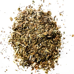 Loose leaf herbal tea blend with dried herbs and plant material scattered on white background, by Yerba Buena Tea Company.