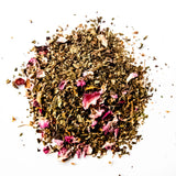 Loose leaf herbal tea blend with dried rose petals scattered on white background, by Yerba Buena Tea Company.