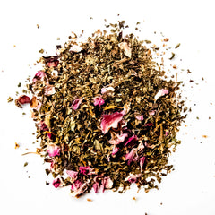 Loose leaf herbal tea blend with dried rose petals scattered on white background, by Yerba Buena Tea Company.